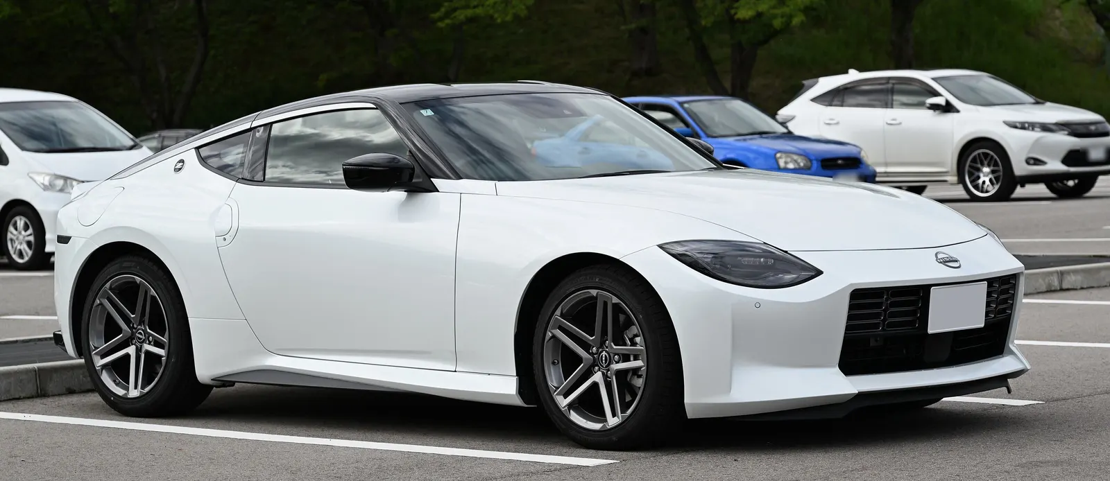 White Nissan Fairlady Z sports coupe parked in an open car park with trees behind