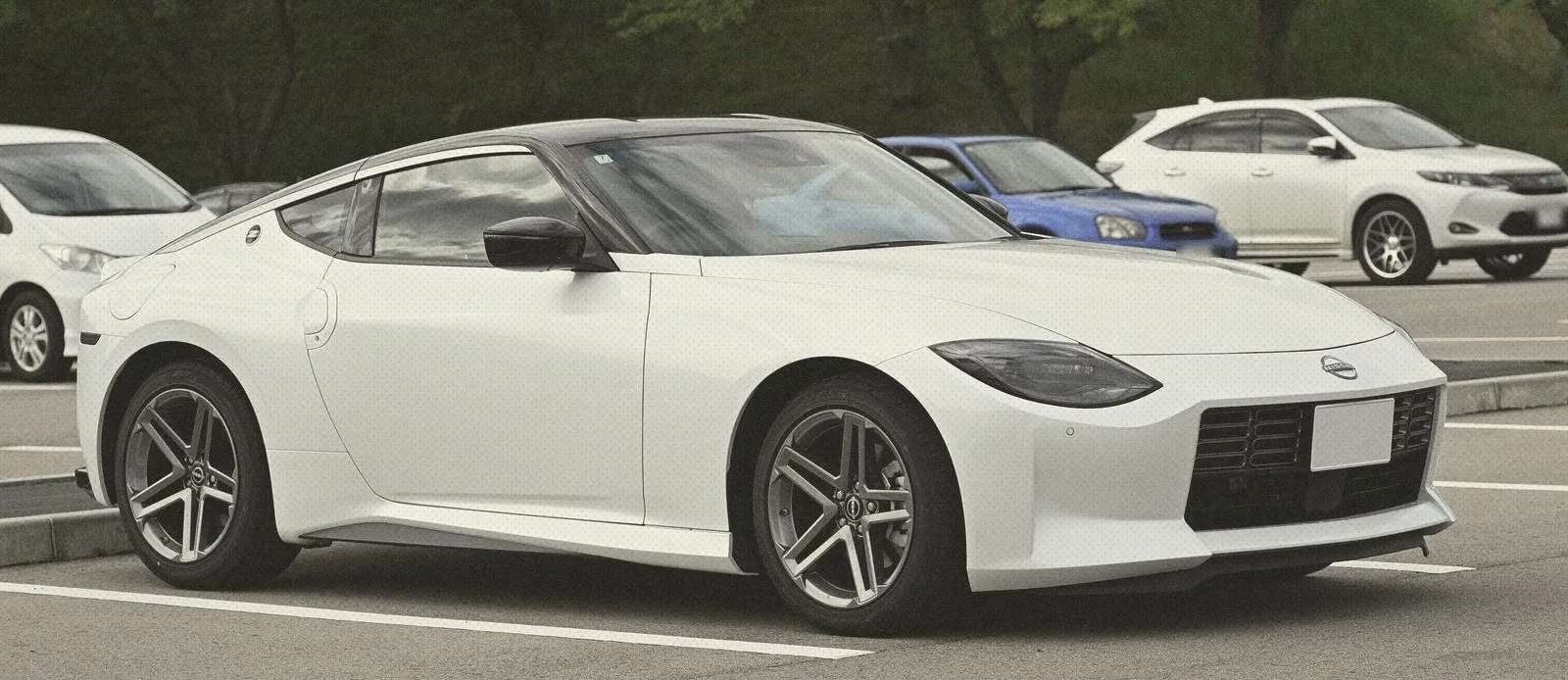 White Nissan Fairlady Z sports coupe parked in an open car park with trees behind