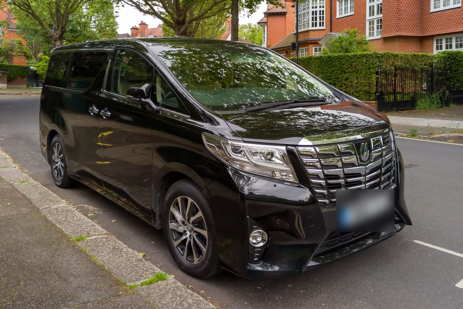 Black Toyota Alphard people carrier parked on a leafy London residential street with red-brick houses behind
