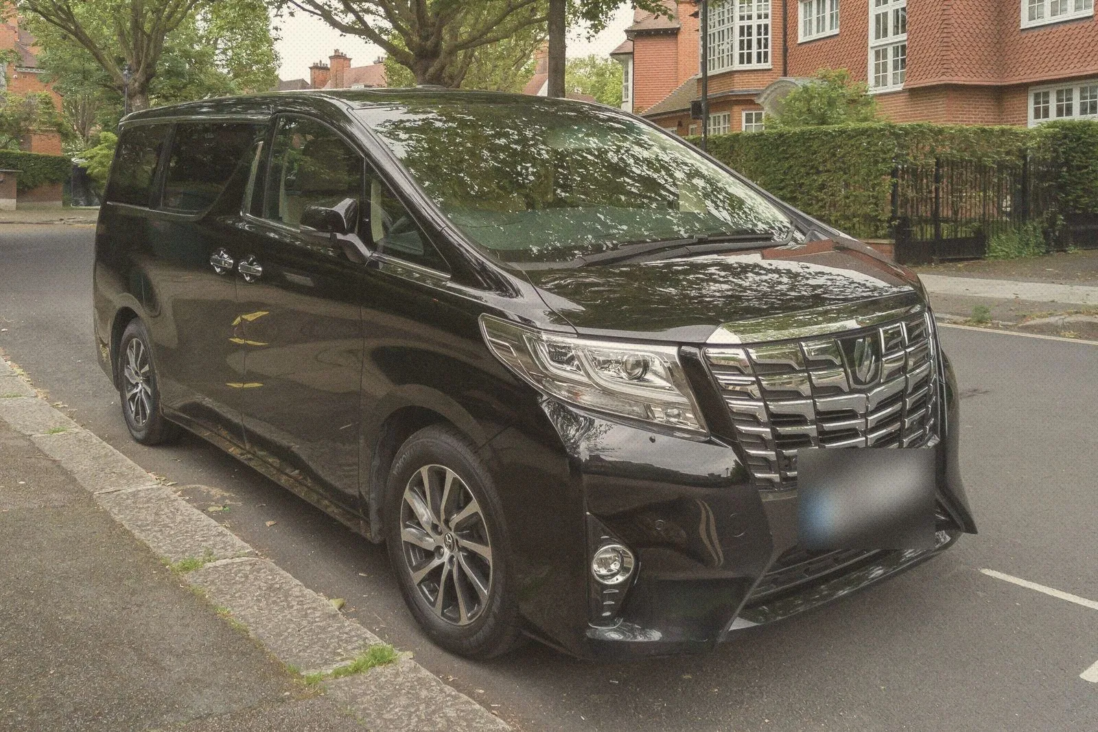 Black Toyota Alphard people carrier parked on a leafy London residential street with red-brick houses behind